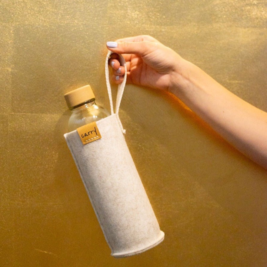 Hand houdt een drinkfles in beige beschermhoes aan de lus vast