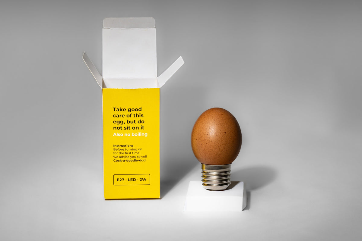 Egglamp Brown op een wit voetje naast de open doos