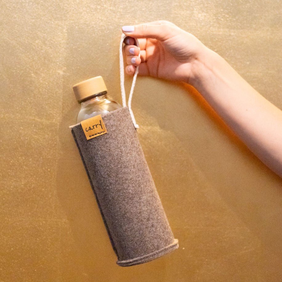 Hand houdt een drinkfles in naturel beschermhoes aan de lus vast