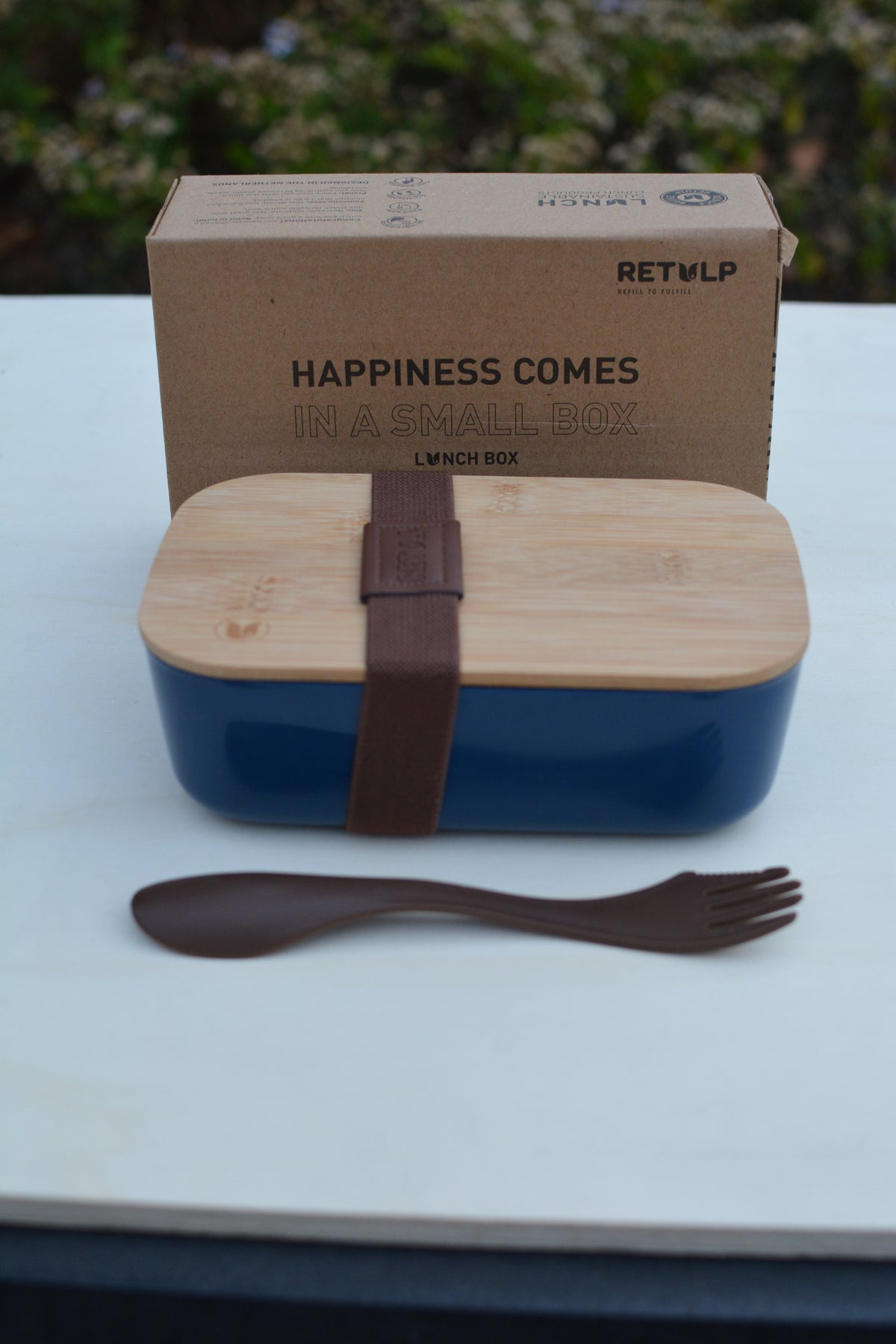 Blauwe lunchbox met bamboe deksel en spork op tafel, met de doos erachter