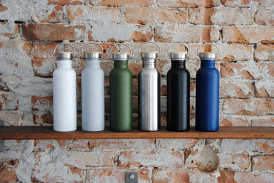 Drinkflessen Urban in verschillende kleuren op een houten plank voor een bakstenen muur