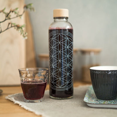 Drinkfles Flower of Life gevuld met een donkere drank, naast een glas en een kop