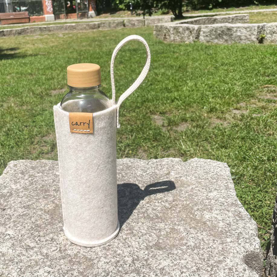 Drinkfles in beige beschermhoes op een steen in het gras