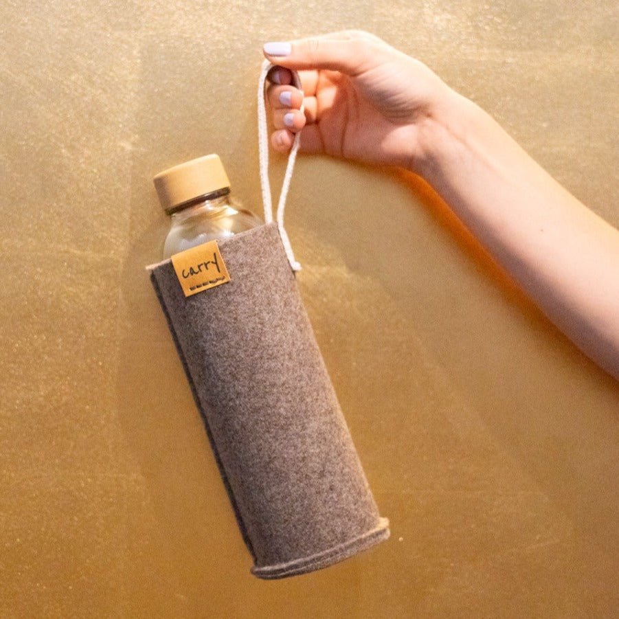 Hand houdt een drinkfles in naturel beschermhoes aan de lus vast