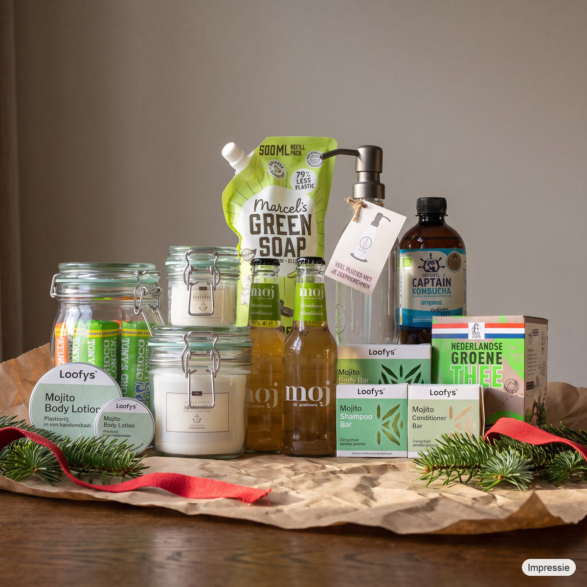 Feel Good Kerstpakket - L - Groen op een houten tafel met kraftpapier, dennentakken en een rood lint (impressie)