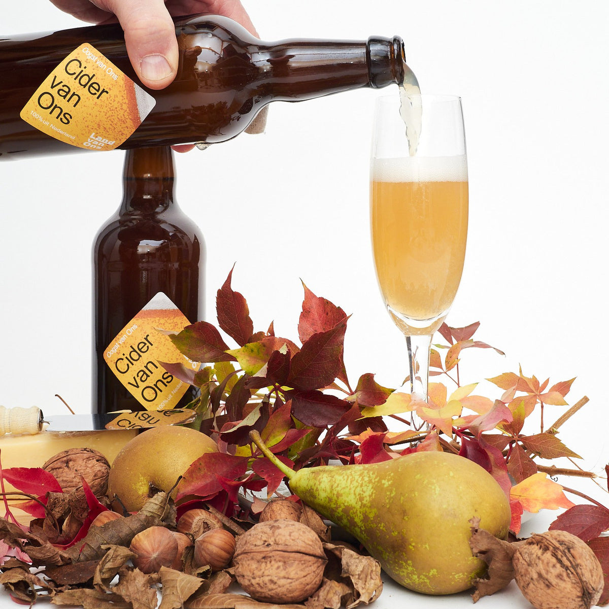 Perencider van Land van Ons wordt in een glas geschonken, tussen peren, noten en herfstbladeren
