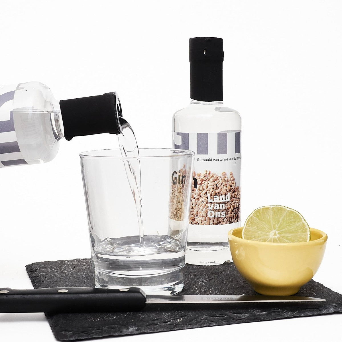 Gin van Land van Ons wordt in een glas geschonken, met een schaaltje limoen